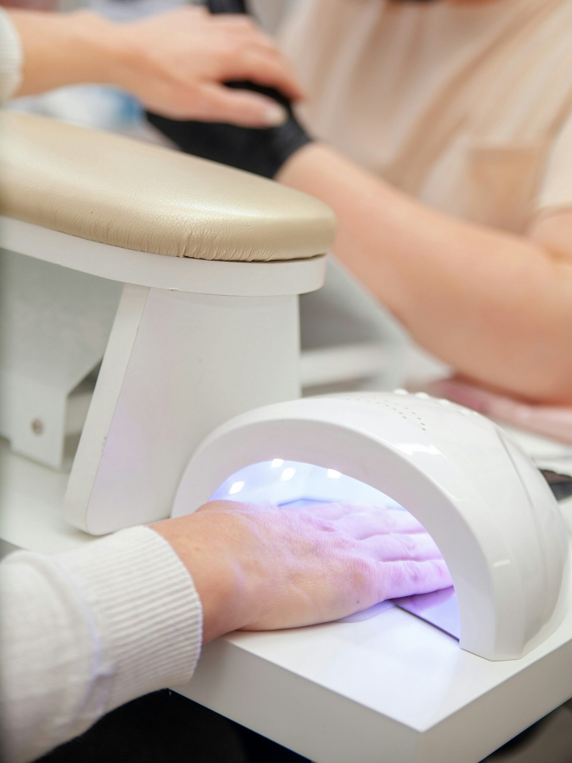 A client in a nail salon curing their BIAB manicure under a UV lamp