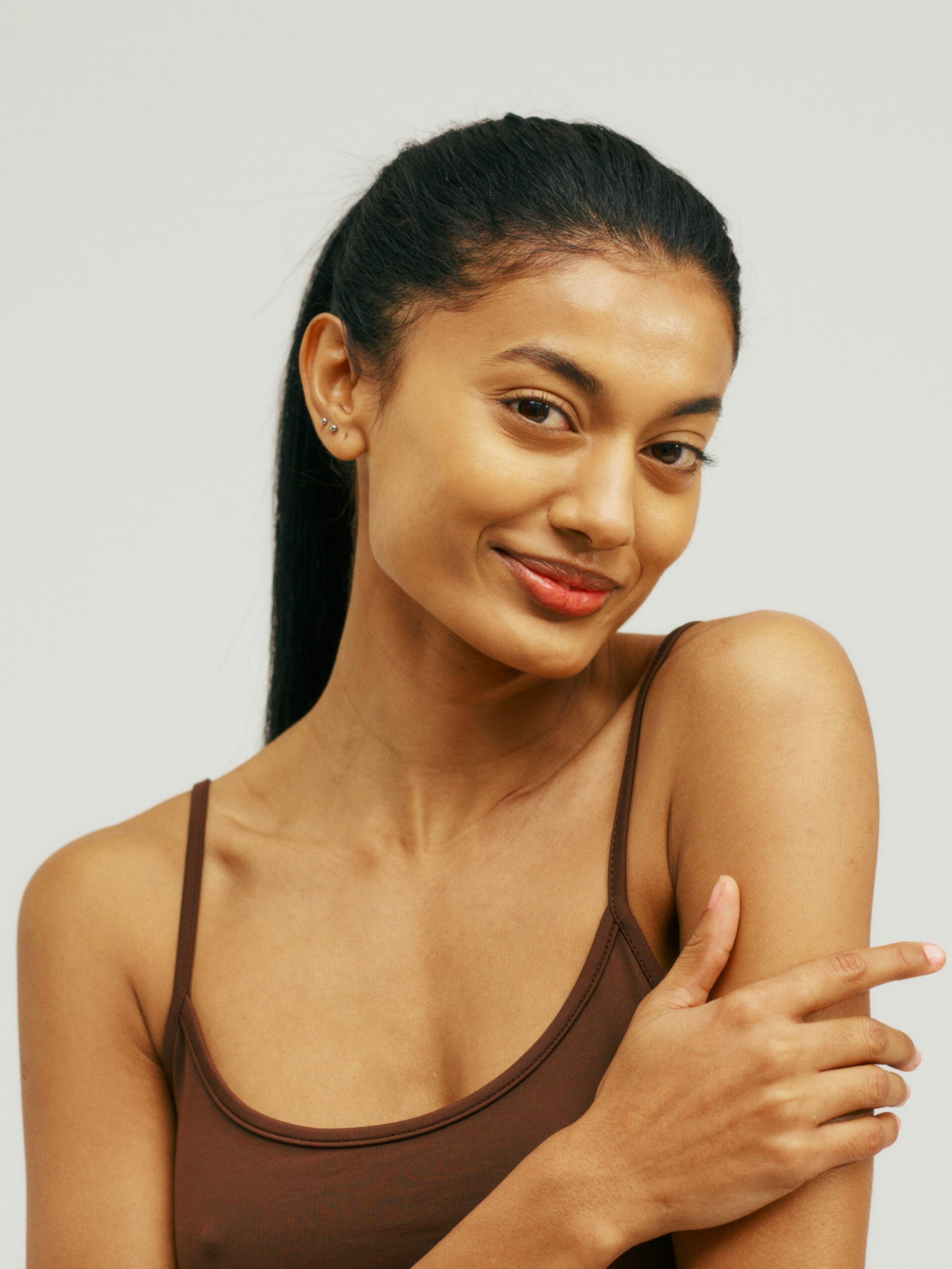 Portrait of a young woman wearing a strappy vest top smiling and stroking her smooth arms