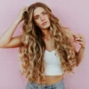 Studio shot of woman with very long, wavy, sun-kissed balayage hair wearing light blue jeans and a white knitted crop top