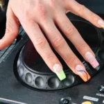 A hand wearing the electric mani on a Pioneer DJ jog wheel, neon French tips in animal print and swirls