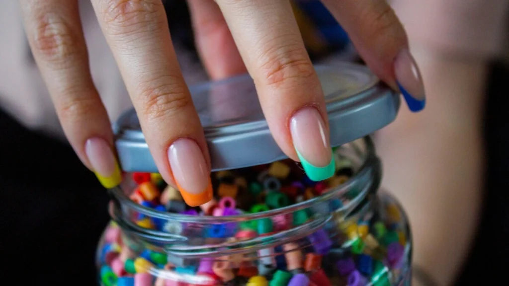 A woman’s hand showing French tips manicure with a sheer nude base and bright multicolored tips