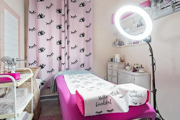 Pink treatment room at Centro Estetico Karma in Olbia with lash-print curtains, a beauty bed and a ring light.