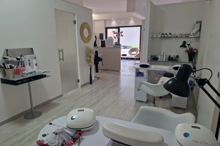 Reception and manicure area at Estetica Francesca in Olbia with a round wall mirror and glass shelving of beauty products.