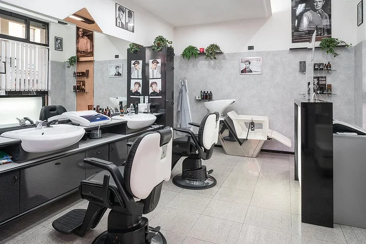Vintage barber chairs and wash stations at Fabio Desole Acconciature Maschili in Sassari with framed portraits on the walls.