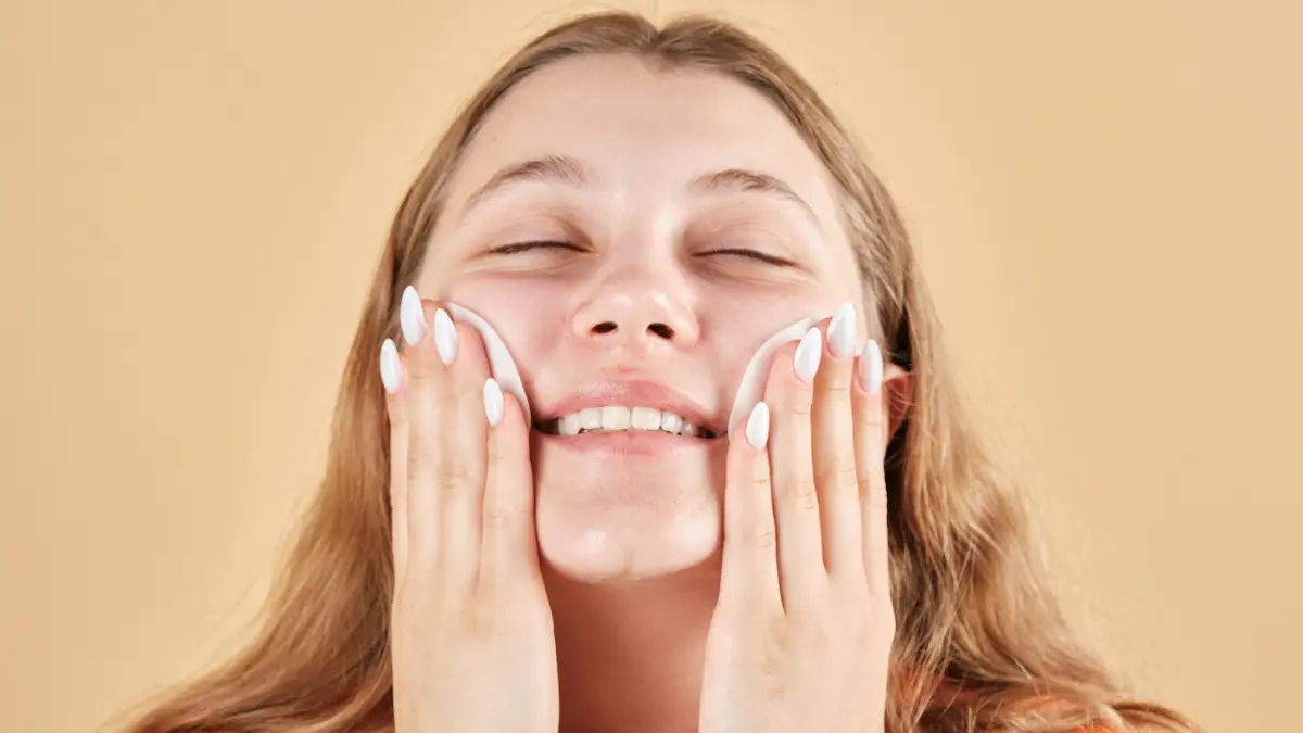 Close-up of a young woman smiling with her eyes closed as she gently wipes her cheeks with cotton pads