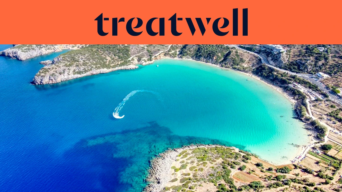 An aerial view of a turquoise Cretan bay, with a jet ski tracing a white curve through clear water, a crescent of sandy beach and dry hills around the shore, beneath a coral-orange banner reading treatwell.