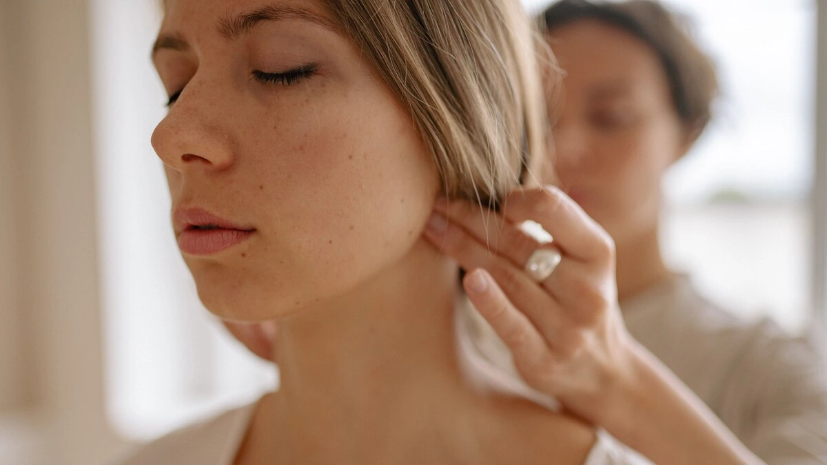Close-up of a woman with her eyes closed as a therapist uses her hands to apply pressure to the base of her skull during an Indian head massage